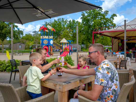 Een familie geniet van een hapje en een drankje op het zonnige terras van het restaurant