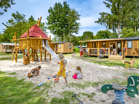 Houten speelhuisjes en diverse speeltoestellen in een grote zandbak op de camping