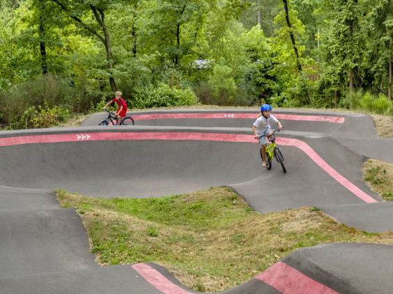 Kinderen rijden met hun fiets over de golvende pumptrack baan in de bosrijke omgeving
