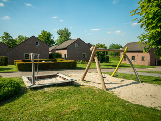 Speeltuintje met schommels en een zandbak, gelegen tussen de vakantiehuisjes van Vakantiepark Reevallis.