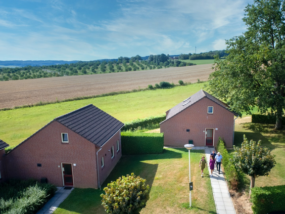 Wandelaars lopen over een pad tussen de vakantiehuizen door, met uitzicht op het heuvelachtige landschap.