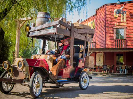 Een gezin maakt een ritje in een oldtimer auto attractie door de Western-straten van Attractiepark Slagharen.