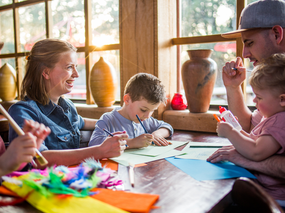 Een gezin met jonge kinderen is gezellig aan het knutselen met gekleurd papier en lijm in een binnenruimte van Vakantiepark Slagharen.