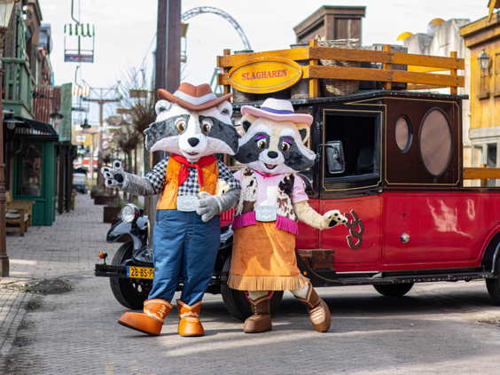 De wasbeer mascottes Randy en Rosie poseren voor hun auto in de hoofdstraat van het Western-gethematiseerde Attractiepark Slagharen.