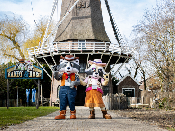 De mascottes Randy en Rosie poseren vrolijk voor een grote, ouderwetse windmolen in Attractiepark Slagharen.