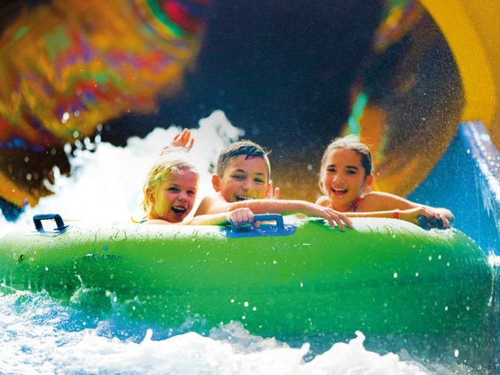 Drie lachende kinderen in een grote groene band roetsjen van een waterglijbaan in Aqua Mexicana, Slagharen.