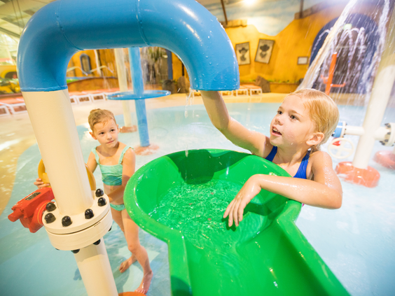 Twee meisjes spelen bij een klein glijbaantje en watersproeiers in het kinderbad van waterpark Aqua Mexicana.