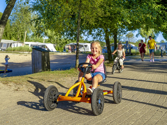 Kind rijdt op een gele skelter over de paden van de camping