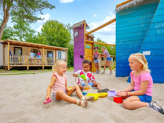Kinderen spelen met zandbakspullen op het brede zandstrand van de camping