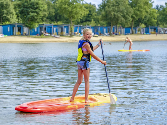 Meisje balanceert op een SUP-board op het rustige water van het meer