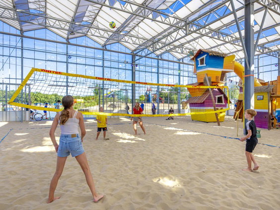 Jongeren spelen beachvolleybal in de grote indoor zandhal Happy Fun Beach op de camping.