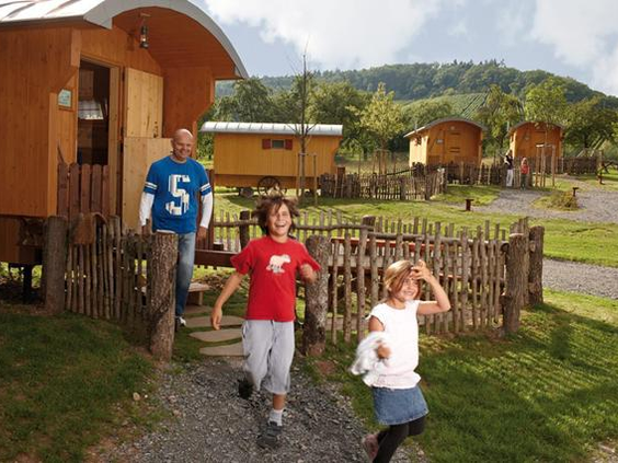 Kinderen rennen vrolijk over een pad naar hun gezellige houten herderswagen op Vakantiepark Tripsdrill.