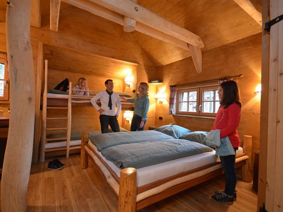 Het ruime en gezellige houten interieur van een boomhut op Vakantiepark Tripsdrill, met een stapelbed, een tweepersoonsbed en een familie.