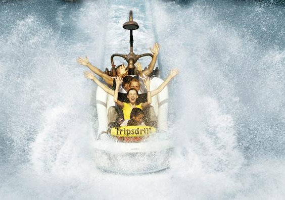 Een groep mensen met hun handen in de lucht in een badkuip-karretje dat met een enorme splash in het water landt in Erlebnispark Tripsdrill.