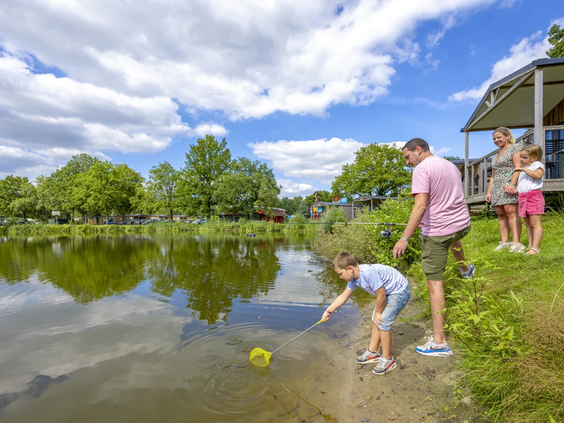 Kinderen spelen bij de waterkant van de vijver onder begeleiding van een volwassene