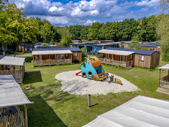 Moderne lodges en chalets gegroepeerd rondom een klein speelveld op de camping