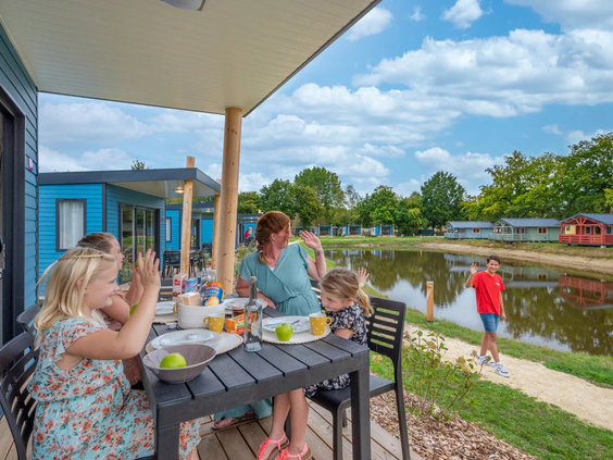 Mensen zitten op het terras met uitzicht op de vijver en lodges