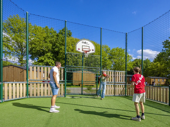 Mensen spelen basketbal op het omheinde multisportveld van de camping
