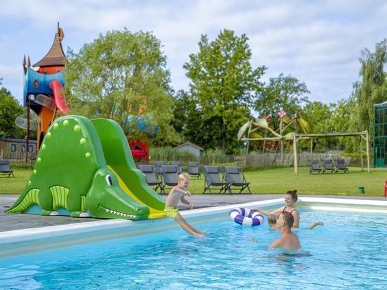 Kinderen spelen in het buitenzwembad bij een groene glijbaan