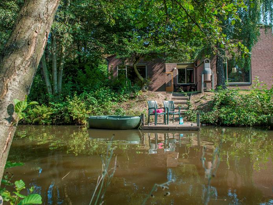 Een bungalow met een vlonder en een eigen roeibootje direct aan het water, omgeven door groen op Vakantiepark Weerterbergen.