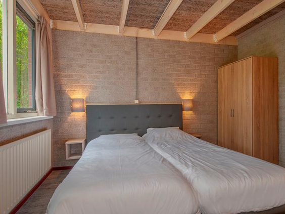 Een netjes opgemaakt tweepersoonsbed in de sfeervolle slaapkamer van een vakantiebungalow op Weerterbergen.