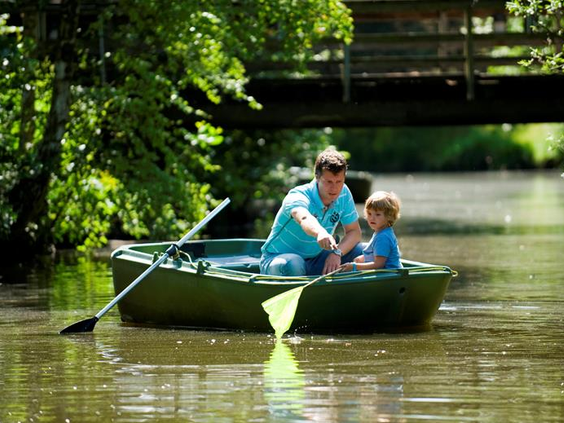 Vader en zoon genieten van een tochtje in een roeiboot op het water tussen de bomen op Vakantiepark Weerterbergen.