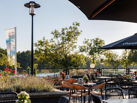Het zonnige terras aan het water van Vakantiepark Weerterbergen, met gezellige zitjes en parasols.
