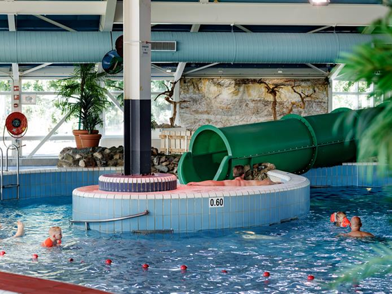 Kinderen hebben plezier bij de grote groene waterglijbaan in het overdekte zwembad van Vakantiepark Weerterbergen in Limburg.