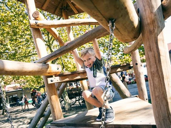 Een jongen klautert in de houten buitenspeeltuin vol uitdagende klimtoestellen op Vakantiepark Weerterbergen.