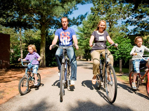 Een gezin met jonge kinderen fietst vrolijk over een pad door de bosrijke omgeving van Vakantiepark Weerterbergen.