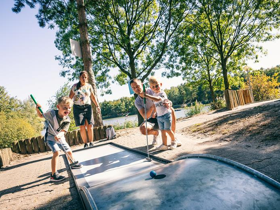 Een gezin geniet samen van een potje midgetgolf op de baan in de buitenlucht bij Vakantiepark Weerterbergen.