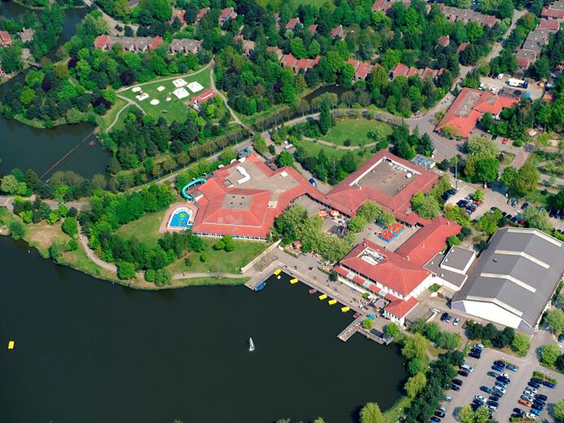 Luchtfoto van Vakantiepark Weerterbergen, met het centrale faciliteitengebouw aan het water, omgeven door groene natuur.