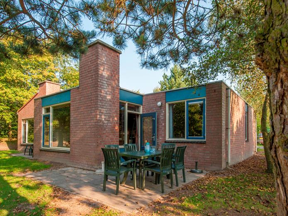 De buitenkant van een vrijstaande, stenen bungalow met terras, gelegen tussen de bomen op Vakantiepark Weerterbergen.