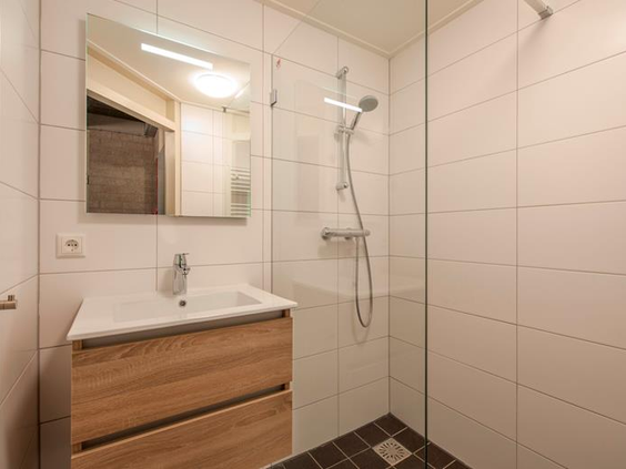 De vernieuwde en moderne badkamer in een bungalow op Weerterbergen, met een inloopdouche en een houten wastafelmeubel.