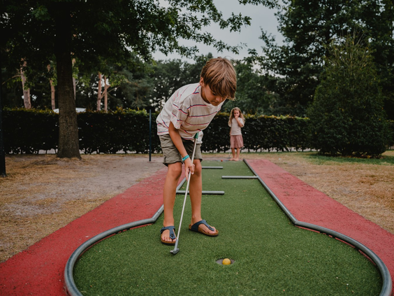 Een jongen concentreert zich terwijl hij een balletje put op de midgetgolfbaan van Vakantiepark Westerbergen.