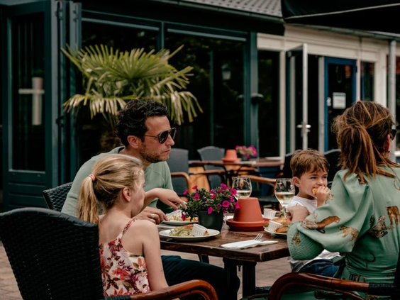 Een gezin met twee kinderen geniet van een gezellige maaltijd op het terras van het restaurant op Vakantiepark Westerbergen.