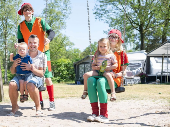 Een gezin gaat lachend op de foto op een schommel samen met twee vrolijke figuren van het animatieteam op Vakantiepark Westerbergen.
