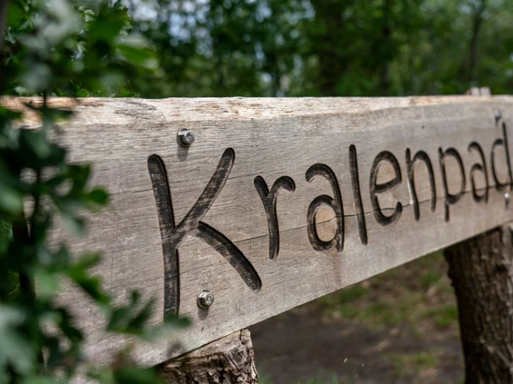 Een houten bord markeert het begin van het Kralenpad, een avontuurlijke kinderwandelroute in de natuur bij Vakantiepark Westerbergen.
