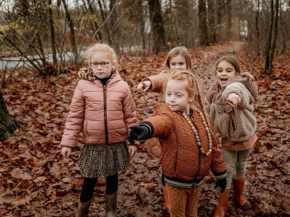 Vier meisjes poseren lachend op een bospad vol herfstbladeren tijdens hun wandeling op het Kralenpad bij Vakantiepark Westerbergen.