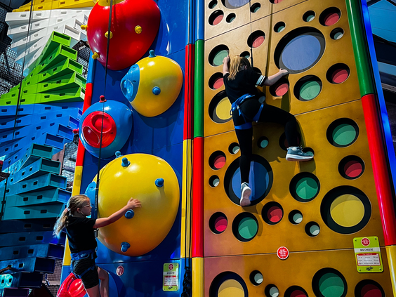 Kinderen met klimgordels klimmen op een kleurrijke en uitdagende indoor klimwand (Clip 'n Climb) bij Vakantiepark Westerbergen.