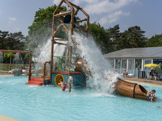 Kinderen spelen in het spraypark met een grote omkiepende emmer en waterglijbaan in het buitenzwembad van Vakantiepark Westerbergen.