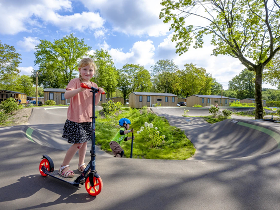 Een kind rijdt op een step over de golvende pumptrack baan