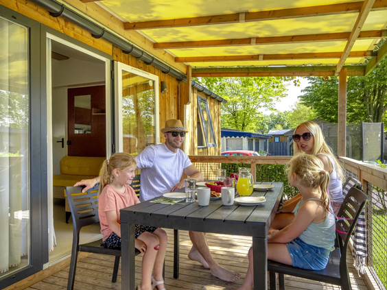 Een gezin zit gezellig aan tafel op de veranda van hun chalet