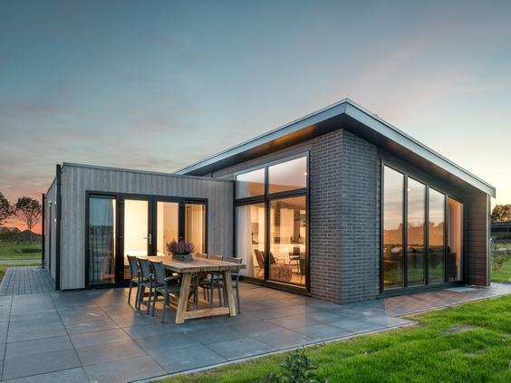 Een luxe, moderne dijklodge op Vakantiepark Zeedijk bij zonsondergang, met een verlicht interieur en een ruim terras in de polder van Zuid-Holland.