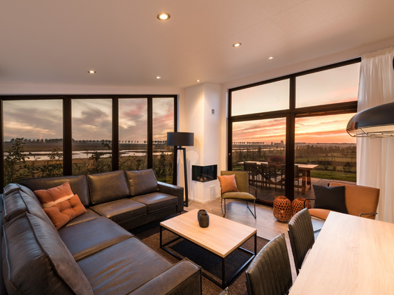Stijlvolle woonkamer in een vakantiehuis op Vakantiepark Zeedijk met een grote hoekbank en een prachtig uitzicht over de polder tijdens zonsondergang.