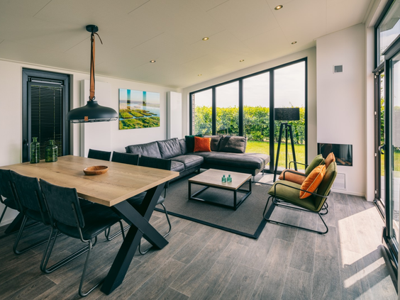 Overzicht van de ruime, modern ingerichte woonkamer met grote ramen die uitkijken op het landschap van Goeree-Overflakkee bij Vakantiepark Zeedijk.