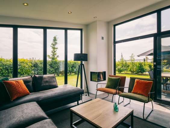 Gezellige zithoek met een comfortabele bank en een moderne haard in een vakantiehuis op Vakantiepark Zeedijk, met uitzicht op de groene omgeving.