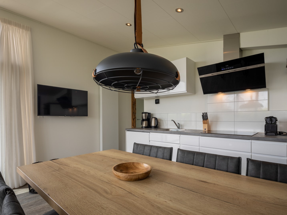 Een grote houten eettafel in de open leefruimte van een vakantiewoning op Vakantiepark Zeedijk, met een moderne keuken op de achtergrond.