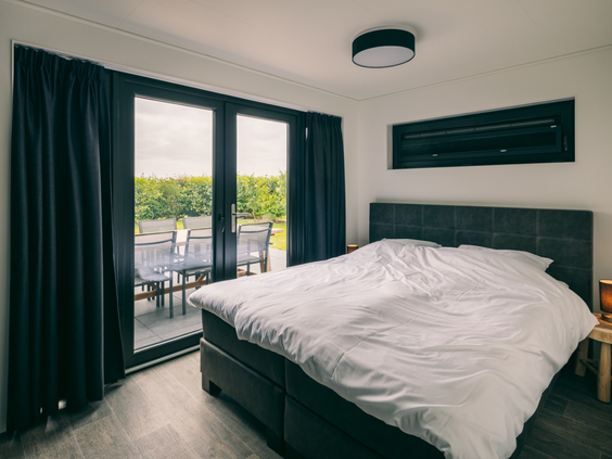 Moderne slaapkamer met een opgemaakt tweepersoonsbed en glazen deuren die openen naar het terras met uitzicht op het polderlandschap.