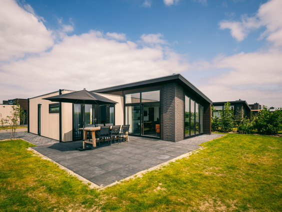 Een moderne, vrijstaande vakantiewoning op Vakantiepark Zeedijk op een zonnige dag, met een groot terras en een tuin direct aan de dijk.